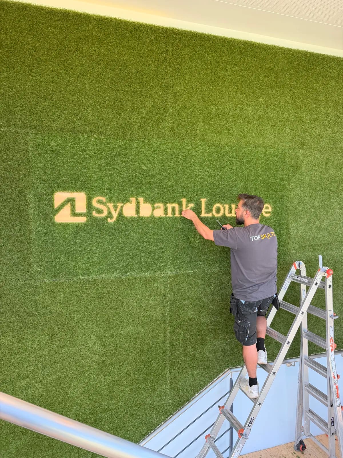 Montage af Sydbank Lounge-logo skåret præcist ind i kunstgræs