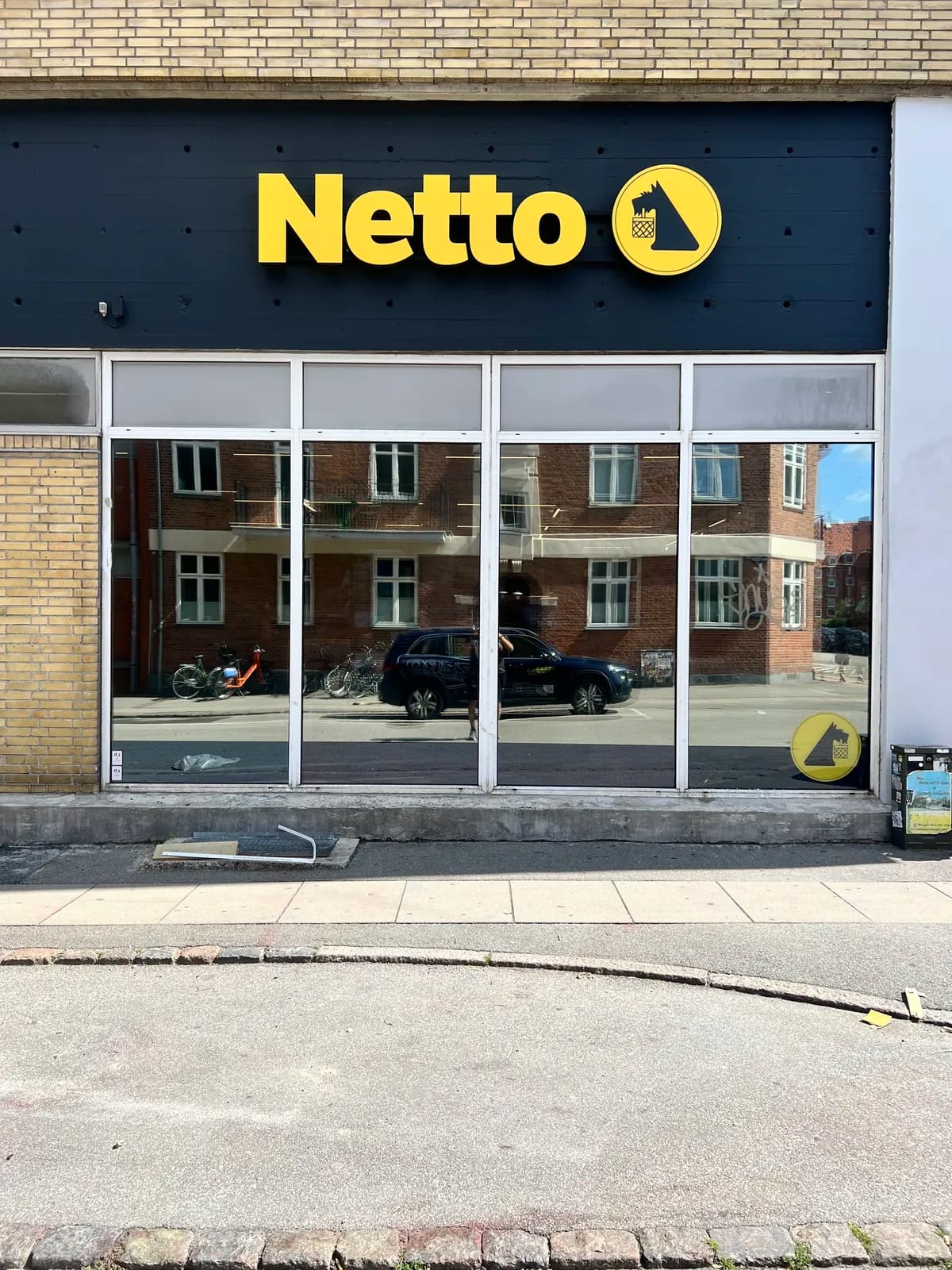 Gule facadebogstaver og rundt logoskilt til Netto monteret på mørk træfacade