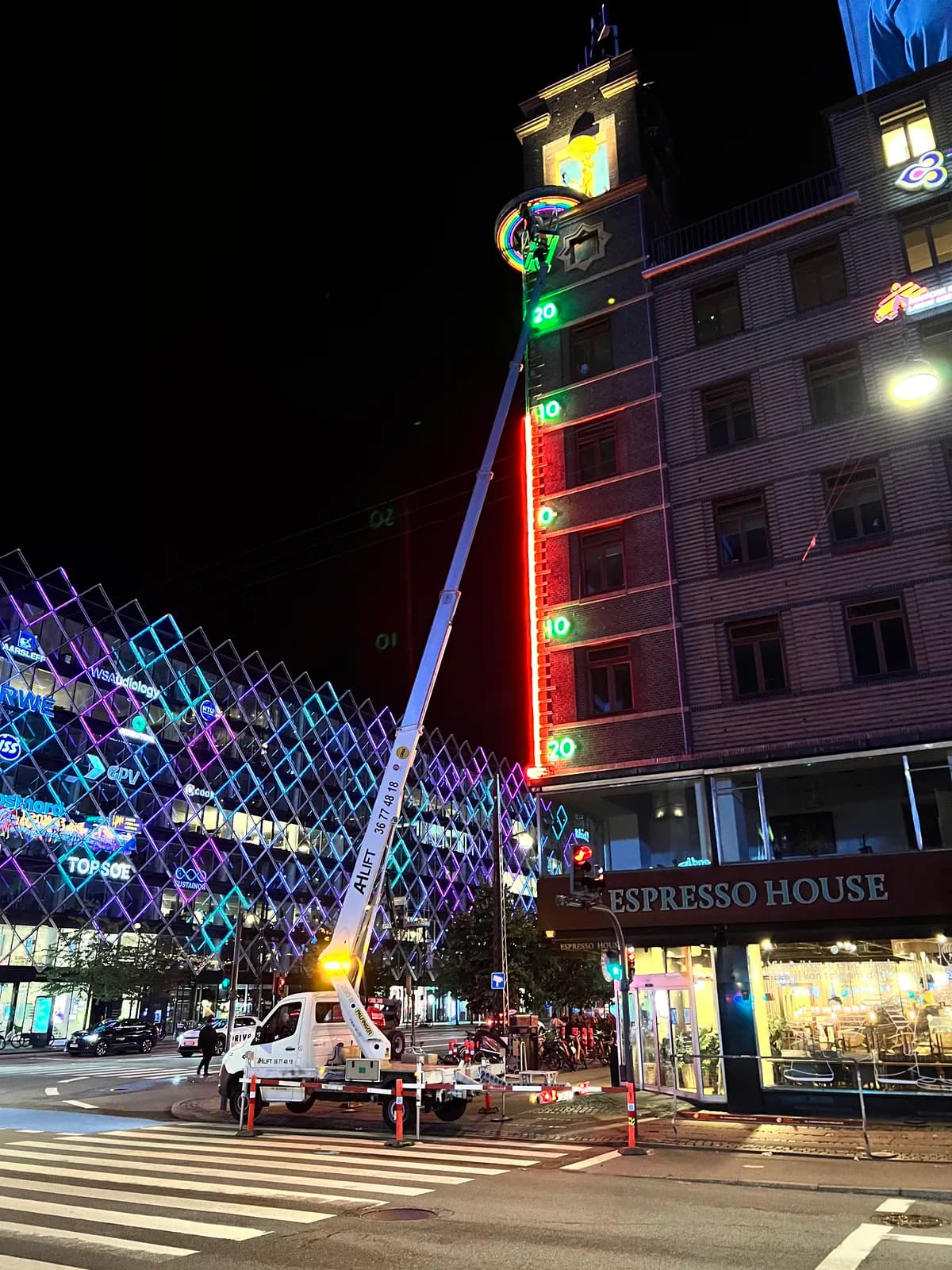 Liftarbejde om natten ved neonskilt med regnbuemotiv på tårnet over Espresso House