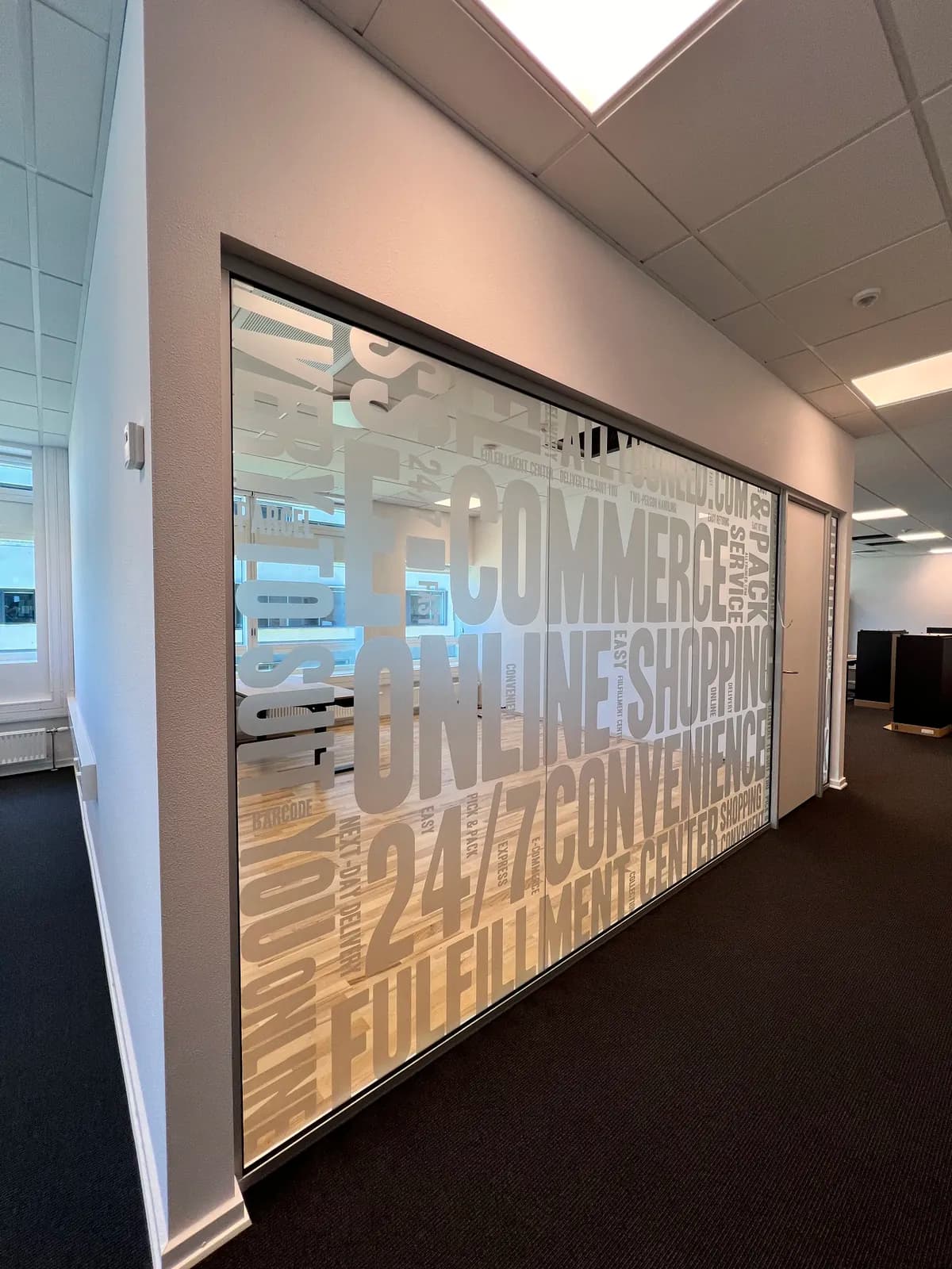 Frostet folie med typografisk e-commerce-motiv monteret på glasvæg i kontormiljø