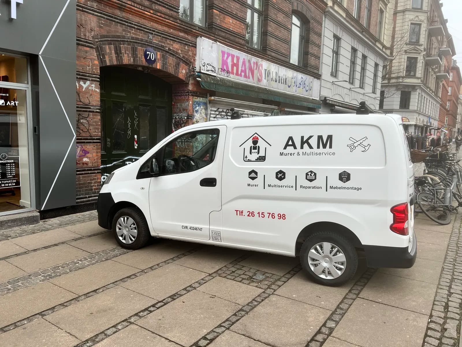 Bildekoration med logo, ydelser og kontaktinfo til AKM Murer & Multiservice på hvid varevogn