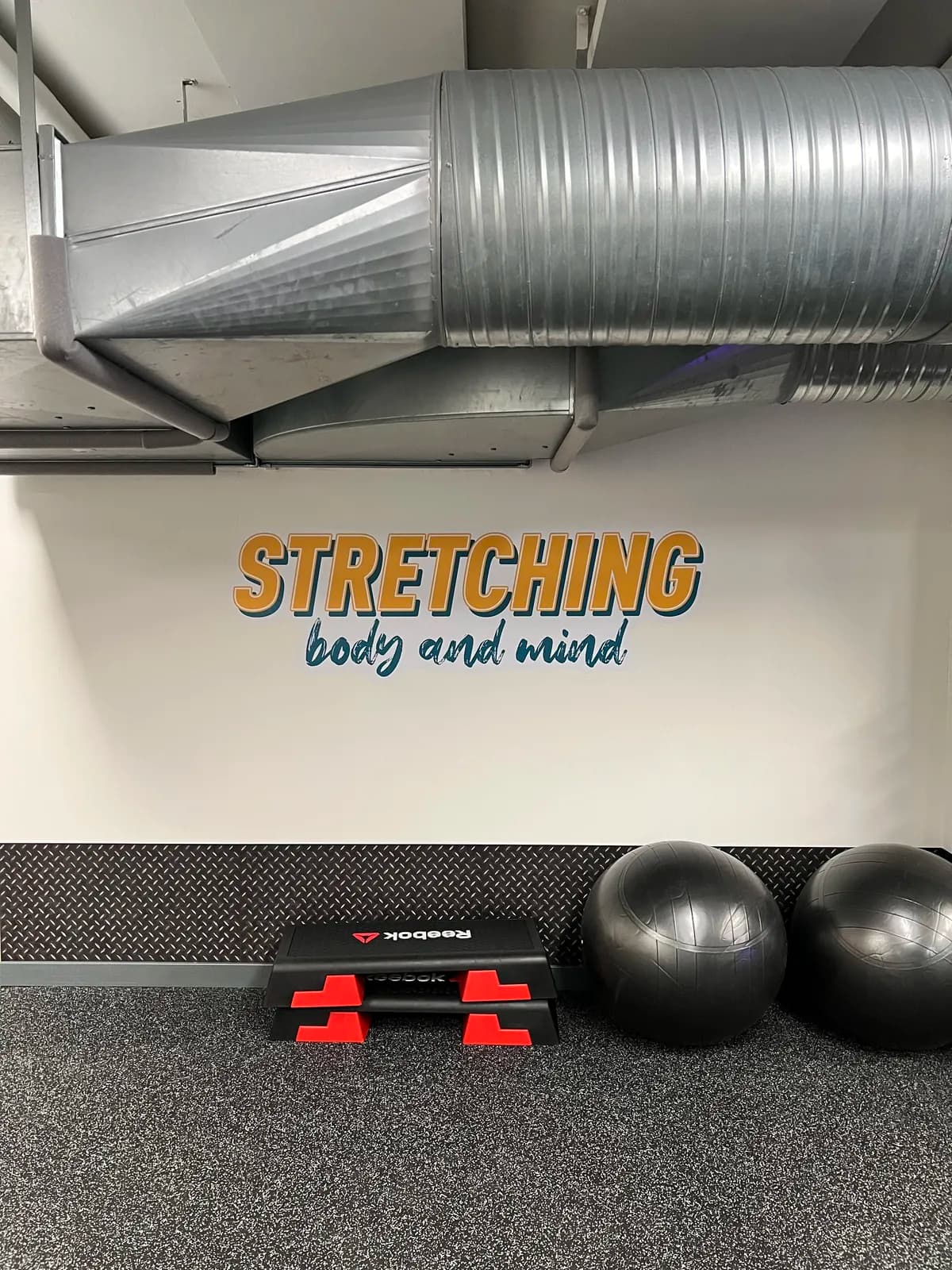 Vægfolie med teksten 'Stretching body and mind' i fitnesscenters udstrækningsområde