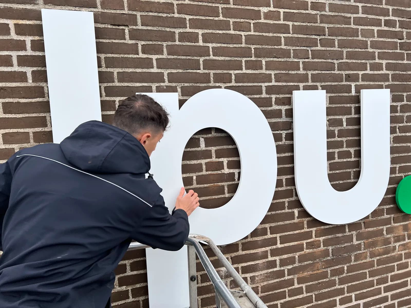 Montage af store hvide facadebogstaver på murstensfacade fra lift