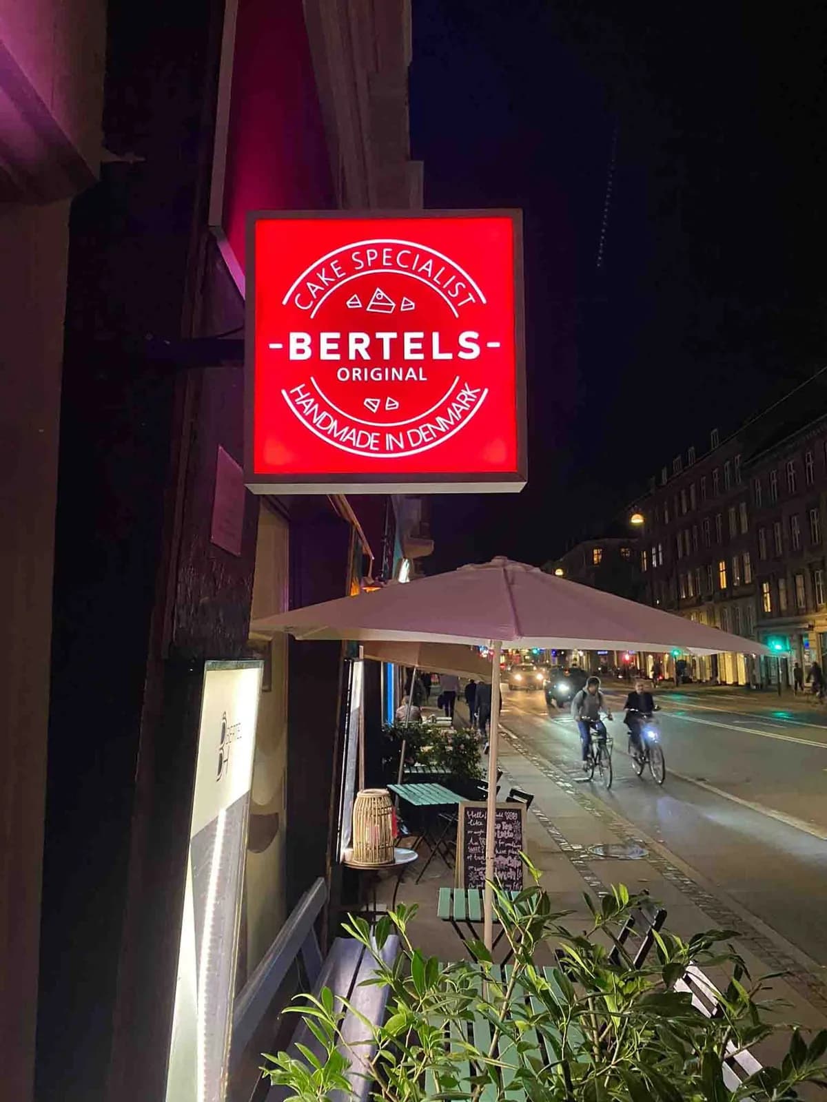 Udhængende lysskilt til Bertels på gågade om aftenen